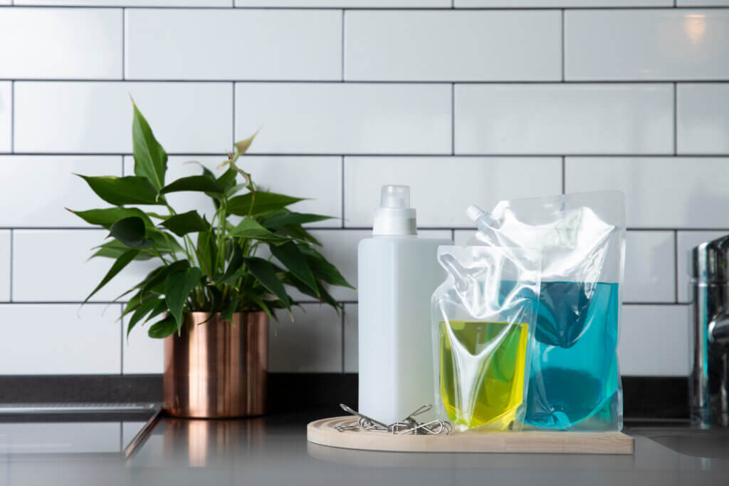Flexible spouted pouches filled with liquid beside a bottle and a plant
